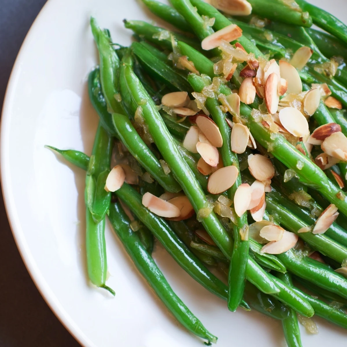 Golden toasted almonds top the freshly plated Green Beans Almondine, hinting at a delicious, savory dish.