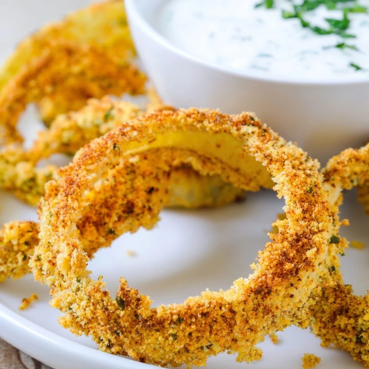 Golden brown Crispy Baked Onion Rings with Ranch piled high, served alongside a creamy dipping sauce for a tasty appetizer.