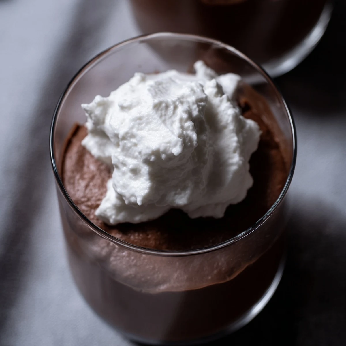 Chocolate Mousse with Homemade Whipped Cream topped with a mint leaf and cocoa powder on a dark plate.