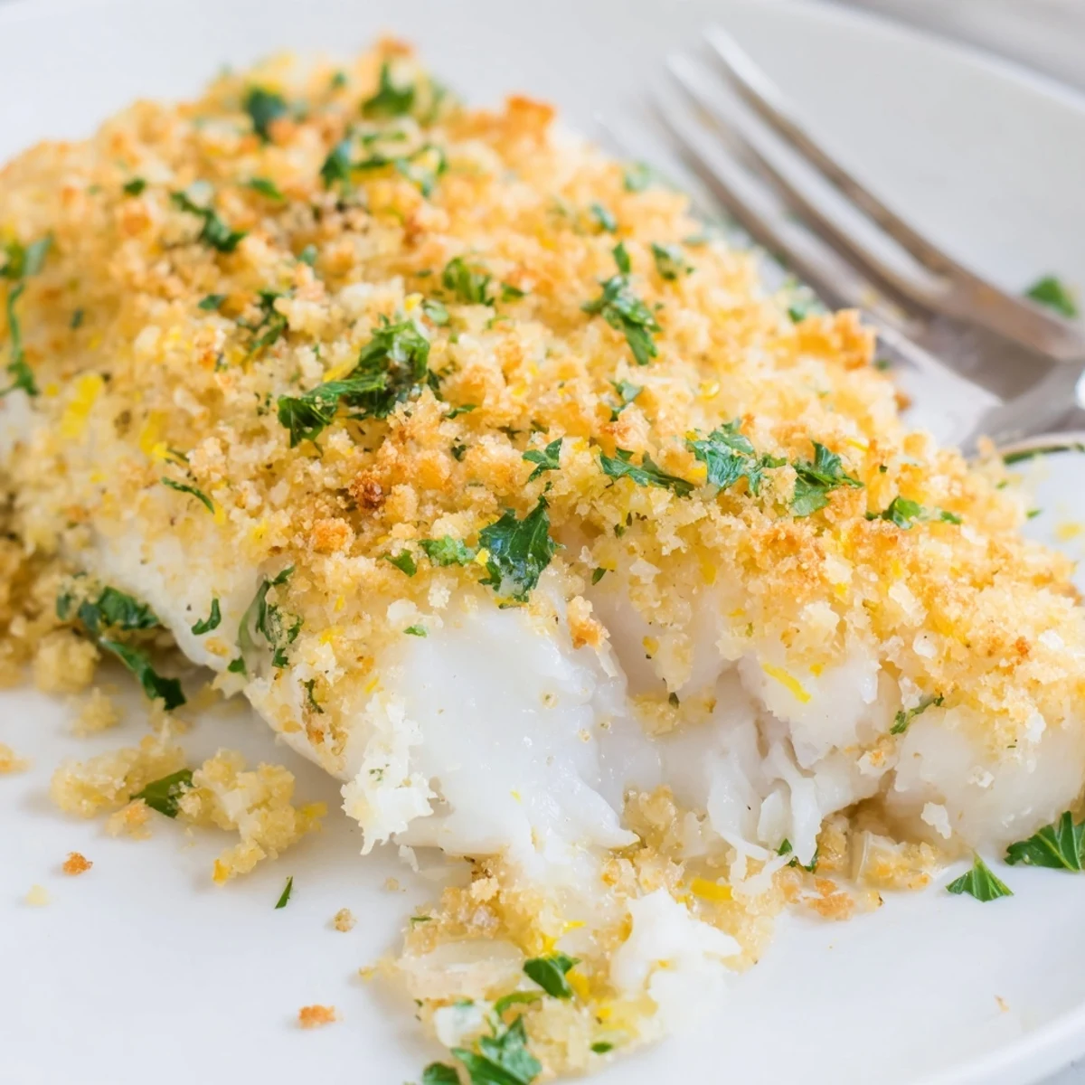 A plated serving of Baked Cod with Buttery Cracker Crumb Topping with lemon wedges and a side salad.
