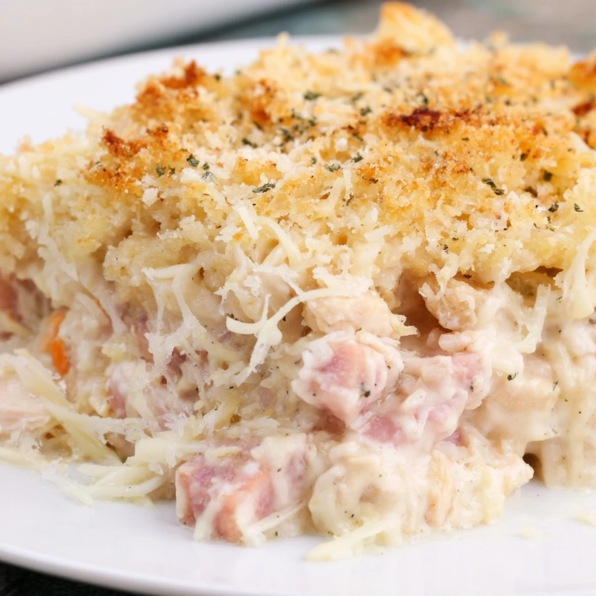 A spoon scoops into a creamy Chicken Cordon Bleu Casserole, revealing layers of shredded halal chicken, diced turkey ham, and rich sauce inside a white ceramic baking dish.