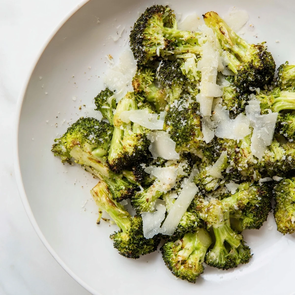 Freshly baked roasted broccoli with garlic and Parmesan cheese served on a plate with lemon wedges.