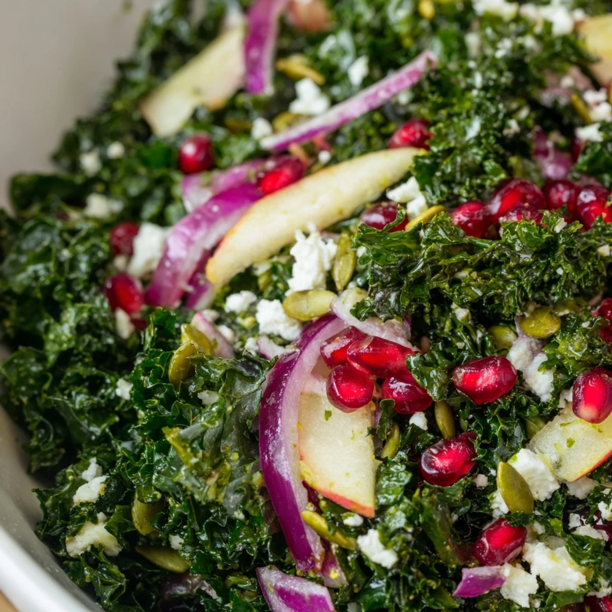 Glistening citrus dressing drizzled over a vibrant Winter Kale Salad with pomegranate seeds and crumbled feta cheese.