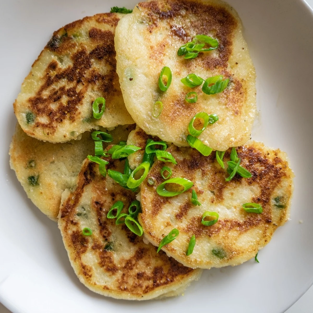 A close-up view of crispy Irish Potato Cakes with Scallions, revealing fluffy interiors flecked with green onions and a pat of melting butter.
