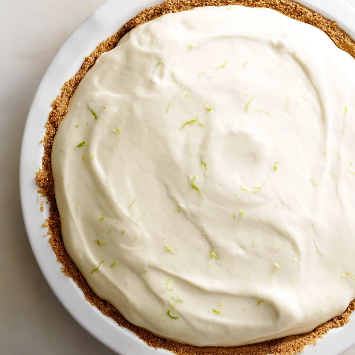 A slice of Key Lime Pie with Whipped Cream Topping on a white plate, featuring a crisp graham cracker crust and a dollop of fluffy cream.