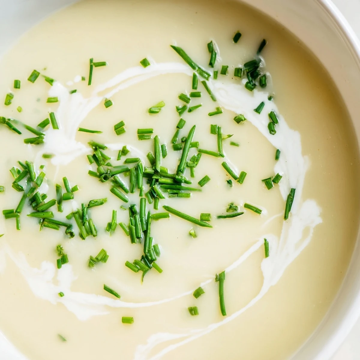 A steaming bowl of creamy potato soup with chives, garnished with a swirl of cream and fresh green herbs.