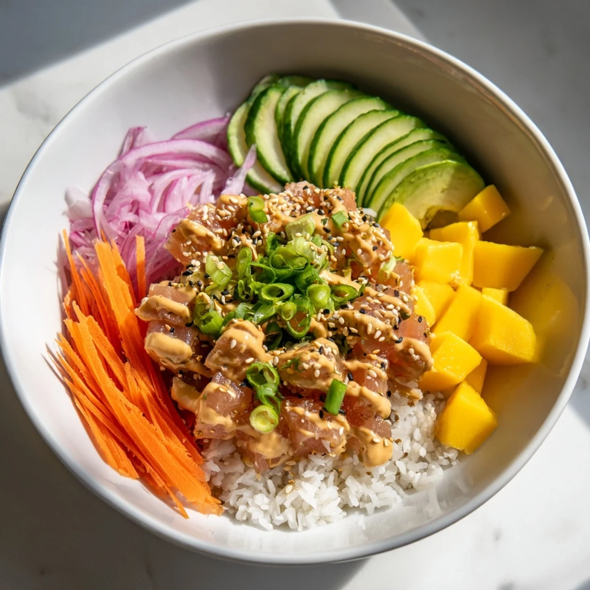Fresh mango cubes and spicy tuna sit atop a bed of fluffy rice with sliced avocado and cucumber.