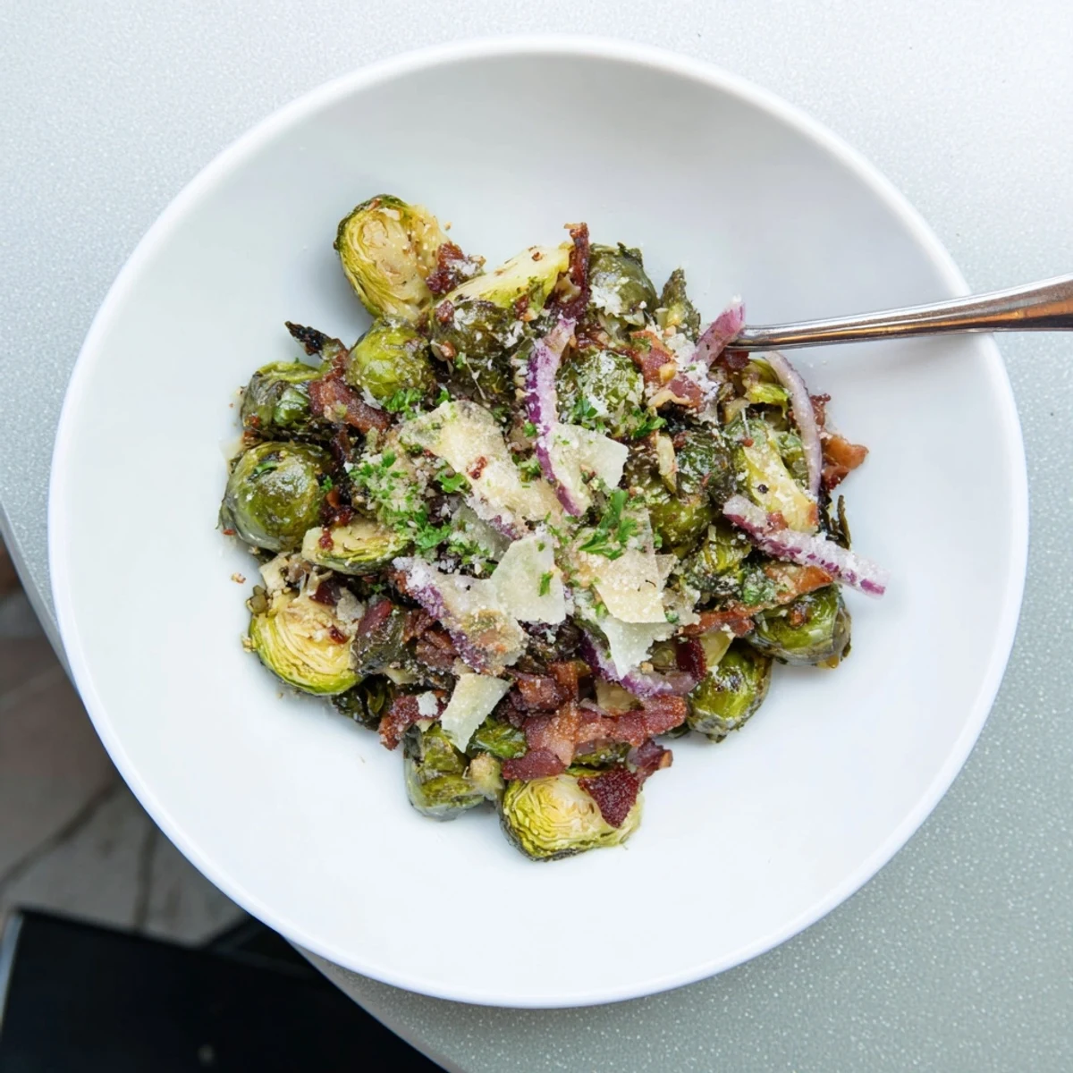 Fresh parsley and grated Parmesan garnish the warm Roasted Brussels Sprouts with Beef Bacon, served on a white plate next to roasted chicken.
