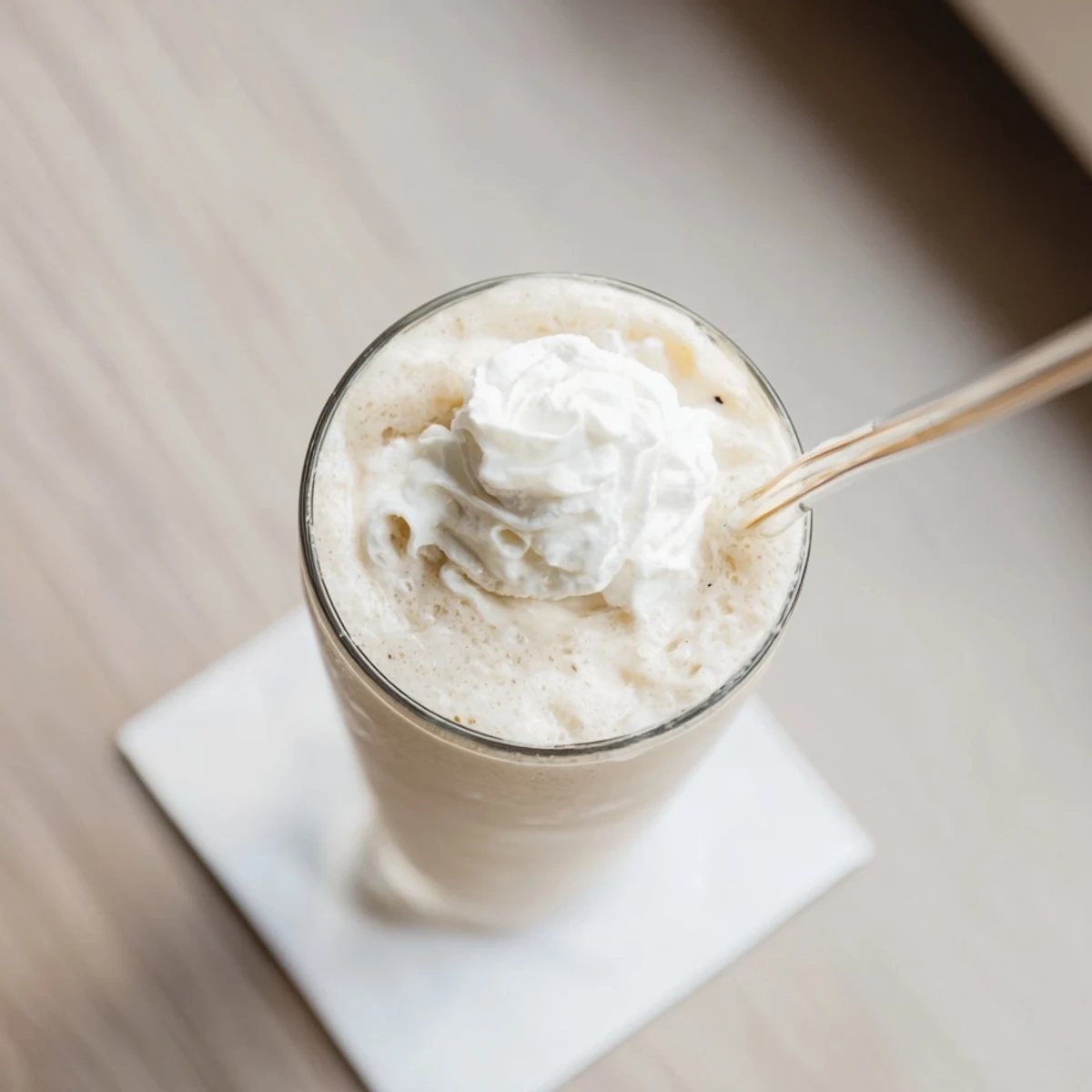 Cold vanilla bean frappuccino with ice cubes, vanilla ice cream, and milk poured into a tall glass.
