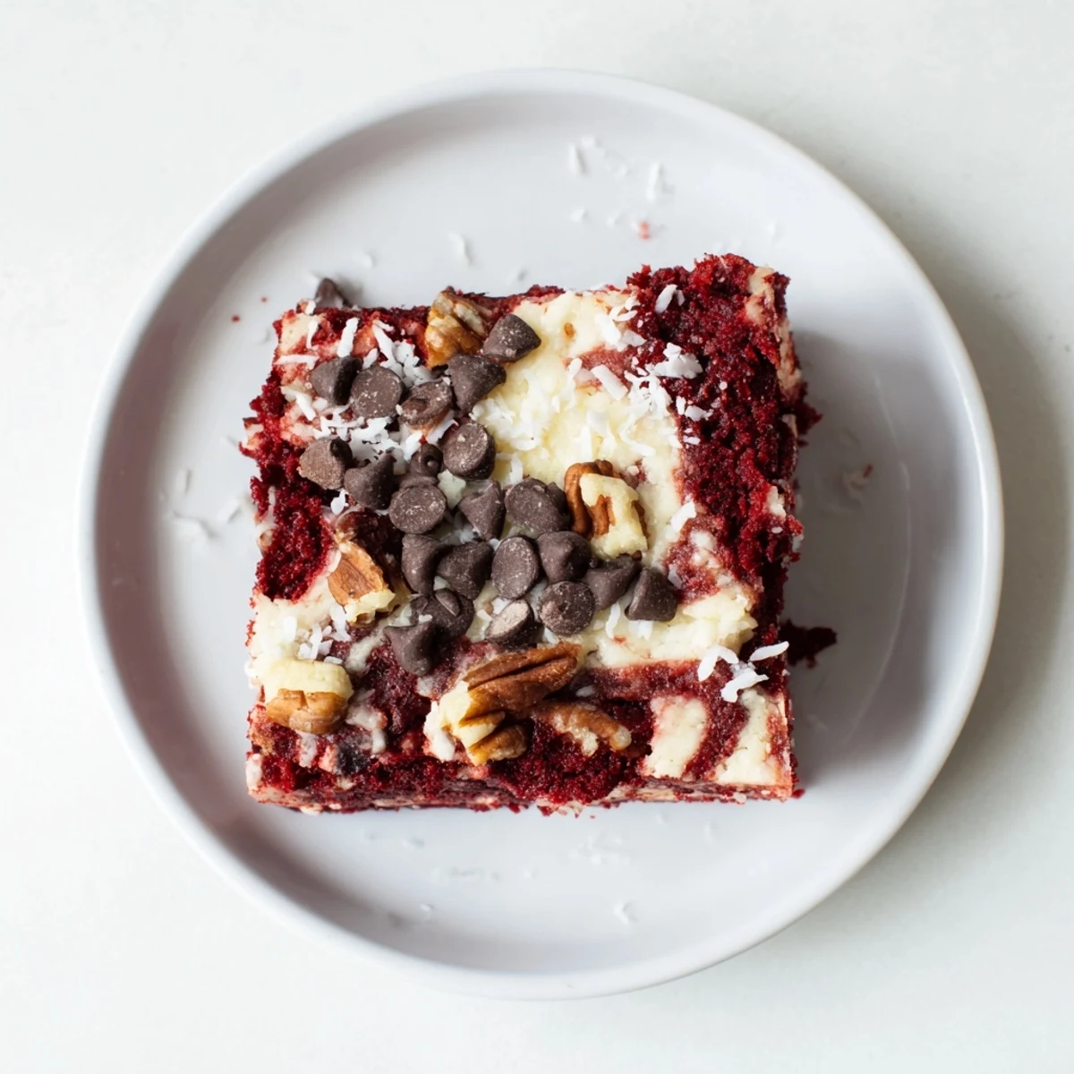 A slice of Red Velvet Earthquake Cake shows rich marbling and melted chocolate chips on a white plate.