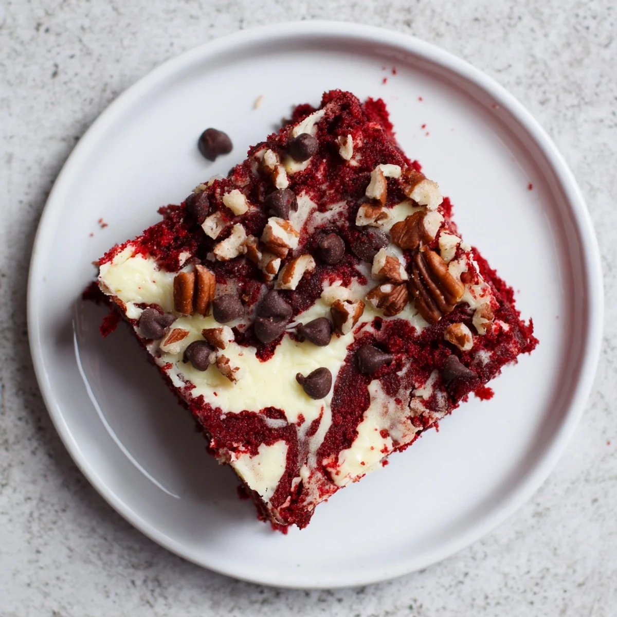 Moist Red Velvet Earthquake Cake with cream cheese swirls and chopped pecans on a rustic wooden board.