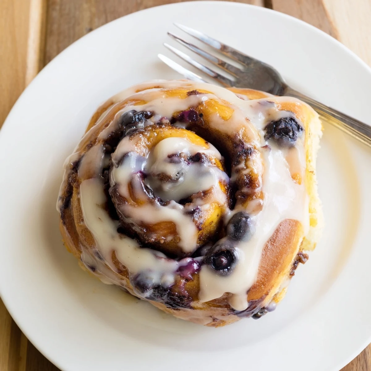 Freshly baked Blueberry Cinnamon Rolls with creamy vanilla glaze on a white plate, ready to eat.