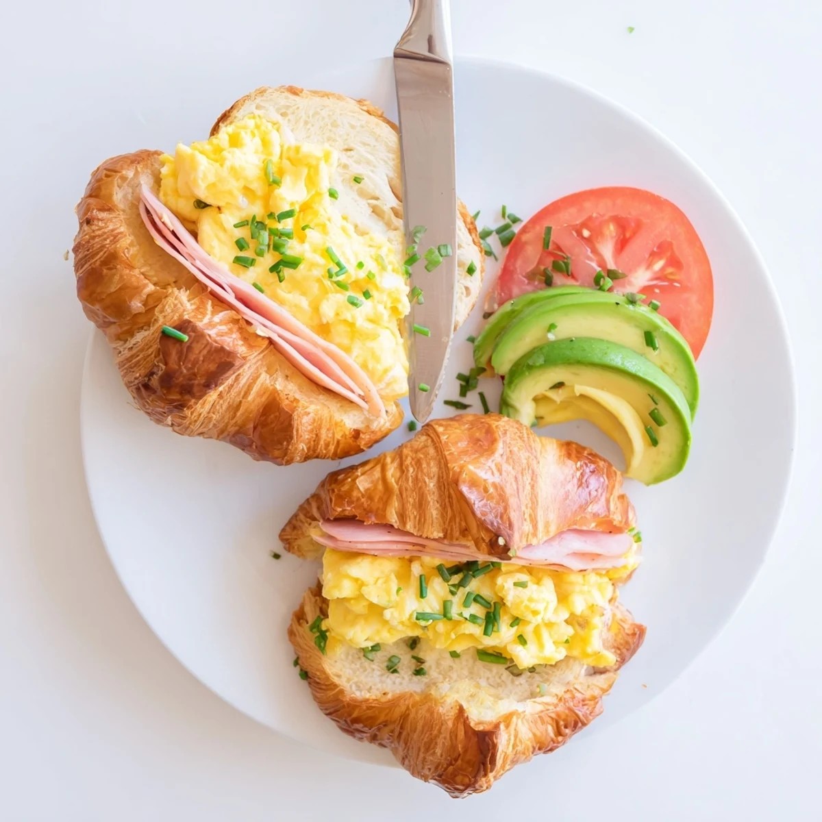 Freshly baked flaky croissant breakfast sandwich bursting with creamy eggs, Swiss cheese, and ripe avocado slices.