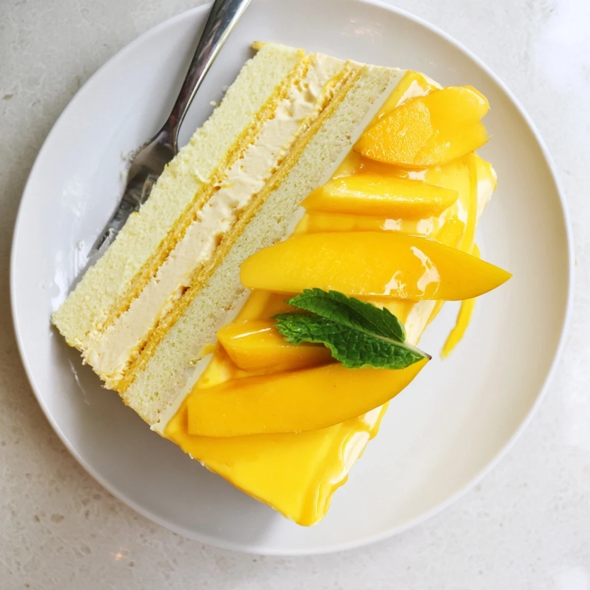 Light and luscious mango mousse cake featuring a fluffy sponge layer, chilled mango glaze, and vibrant tropical fruit garnish.  