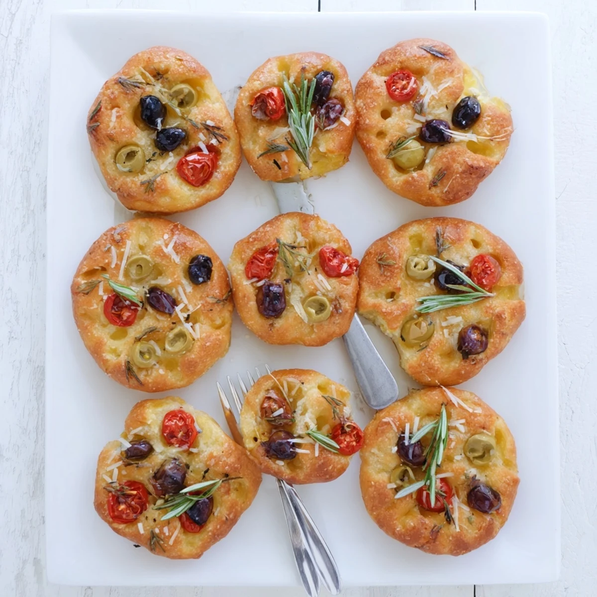 Golden crispy mini focaccia topped with fresh rosemary flaky sea salt and olive oil on a wooden board