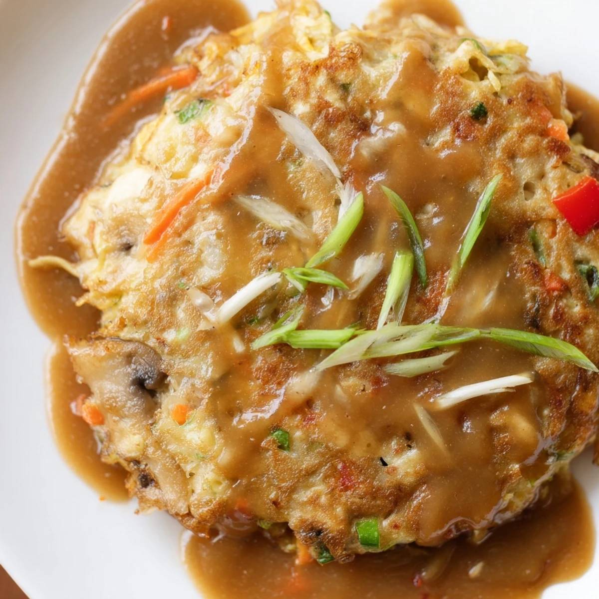 Golden crispy Egg Foo Young patties drizzled with savory brown gravy on white plate