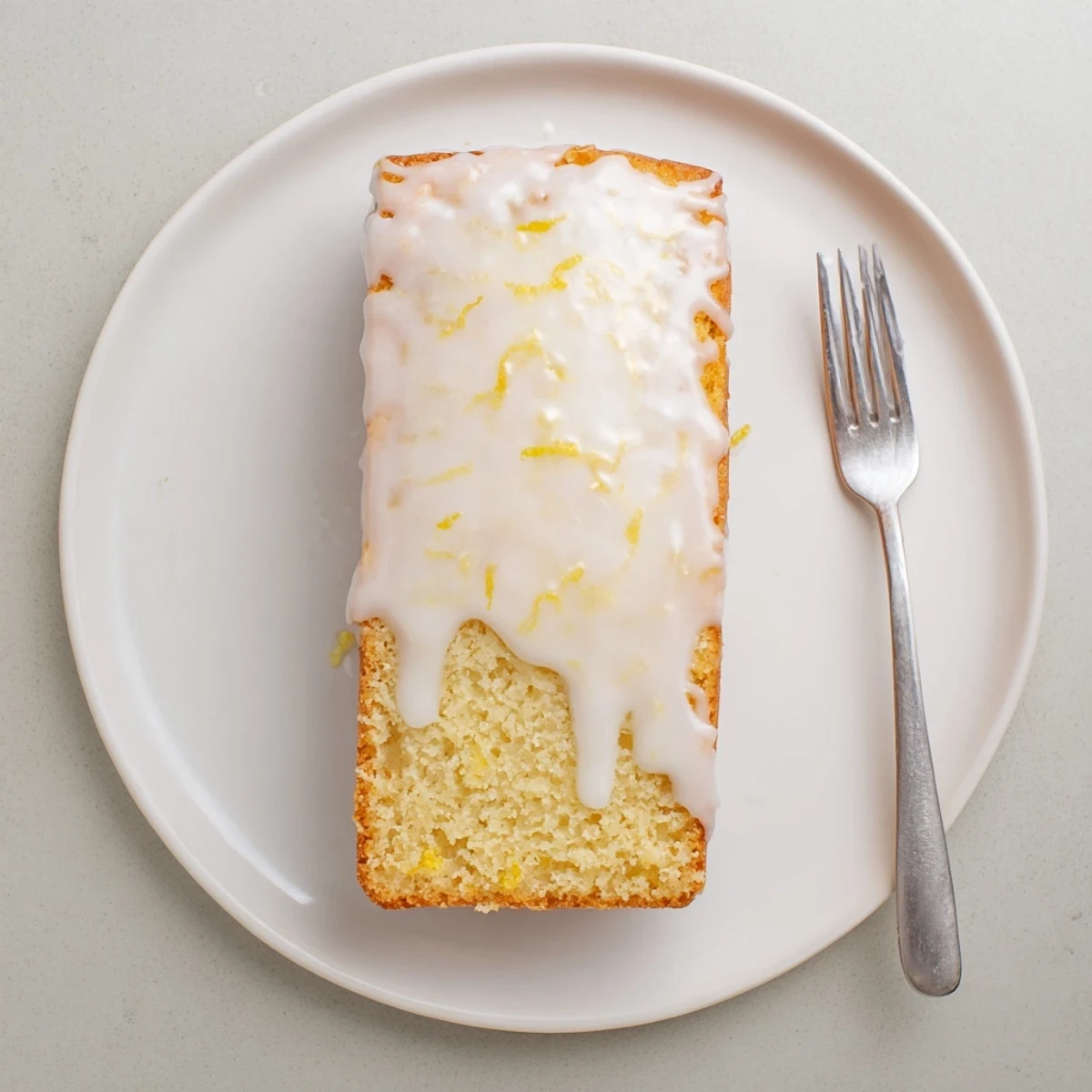 Moist lemon loaf cake drizzled with tangy citrus glaze on a white serving plate