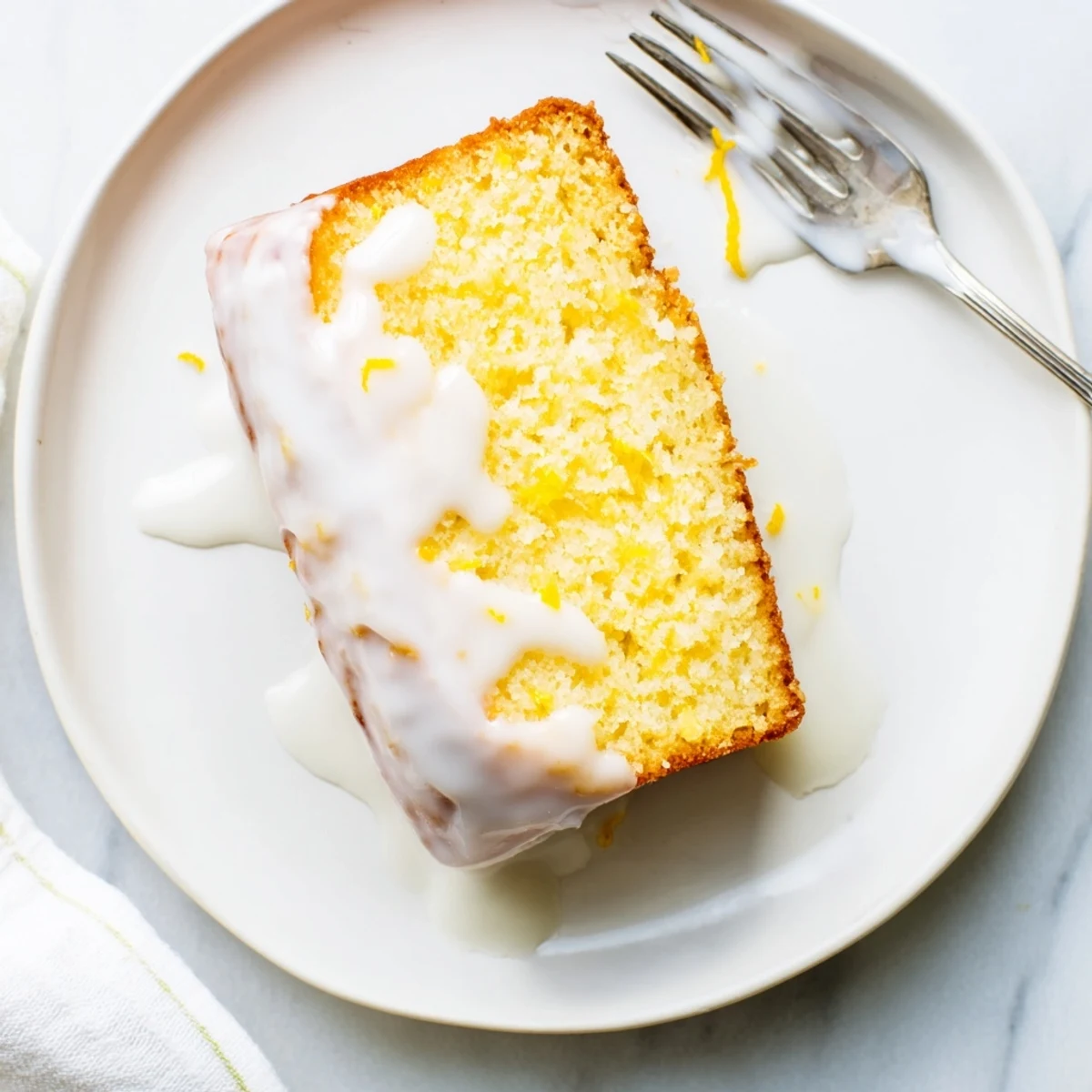 Golden lemon loaf slice topped with zesty glaze and fresh lemon zest garnish
