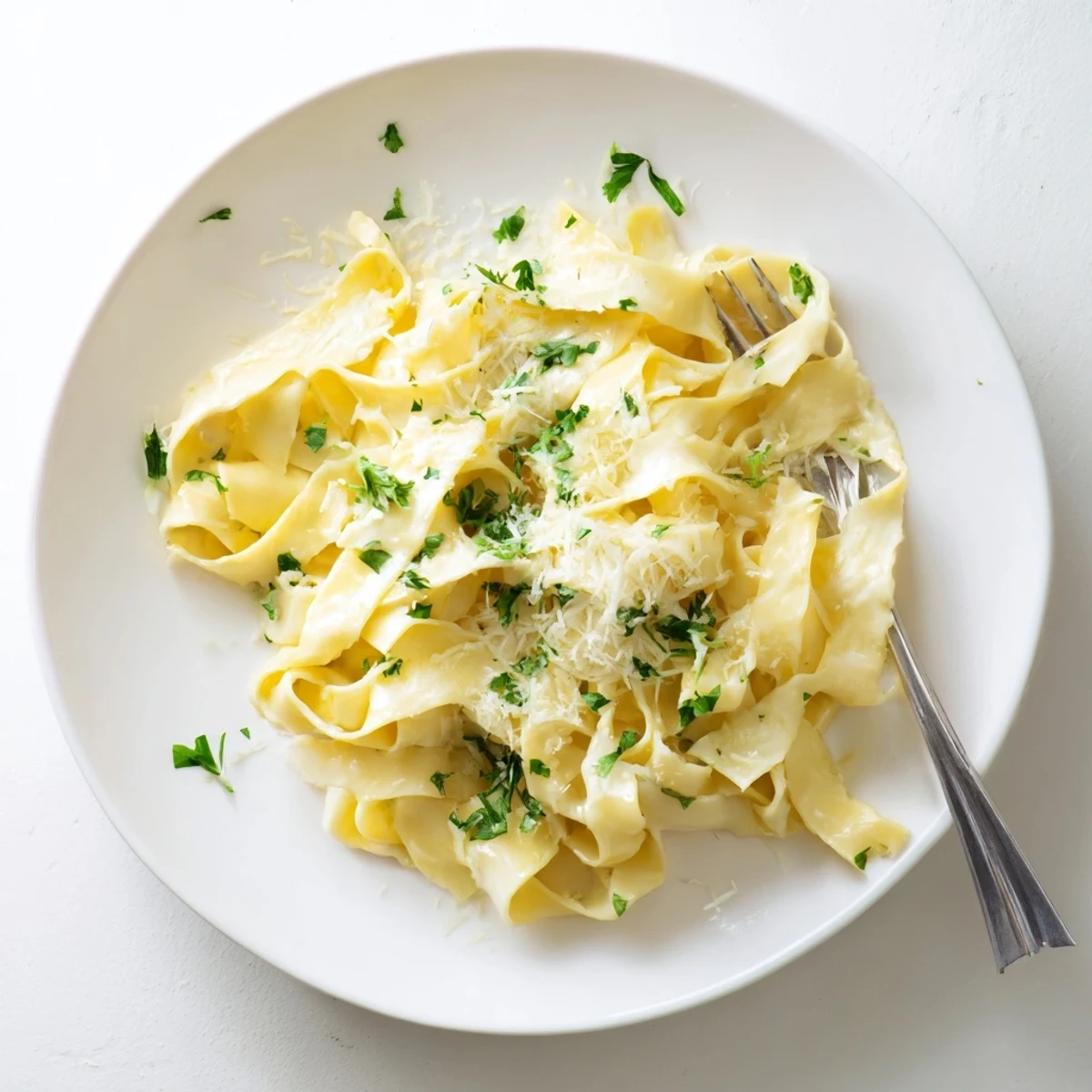 Creamy Alfredo pasta tossed with buttery Parmesan sauce on white dinner plate