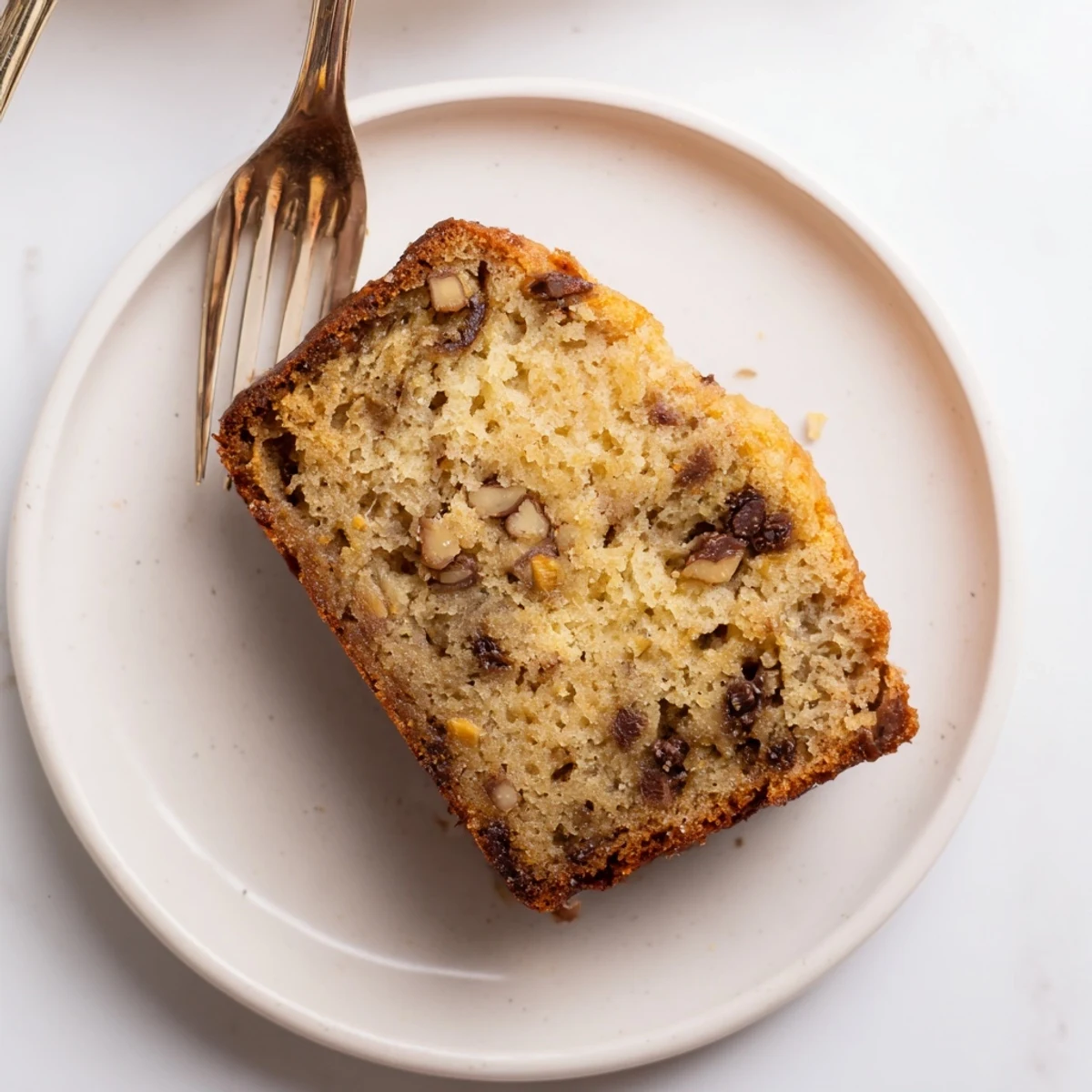 Thick slice of super moist banana bread revealing tender crumb, served on a white plate with scattered walnut pieces