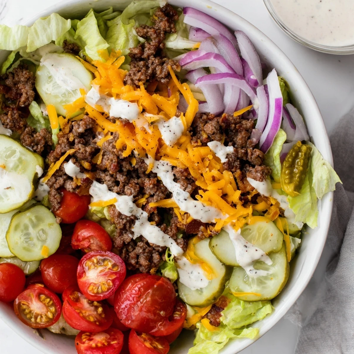 Layered burger bowls displaying ground beef crumbles, shredded cheese, crisp vegetables, and tangy sauce in a serving bowl