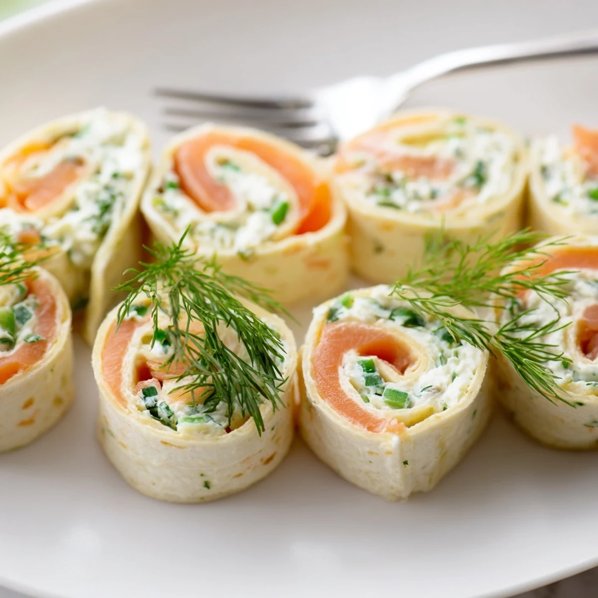 Spiral slices of smoked salmon roll ups filled with herbed cream cheese and fresh dill on a white serving platter