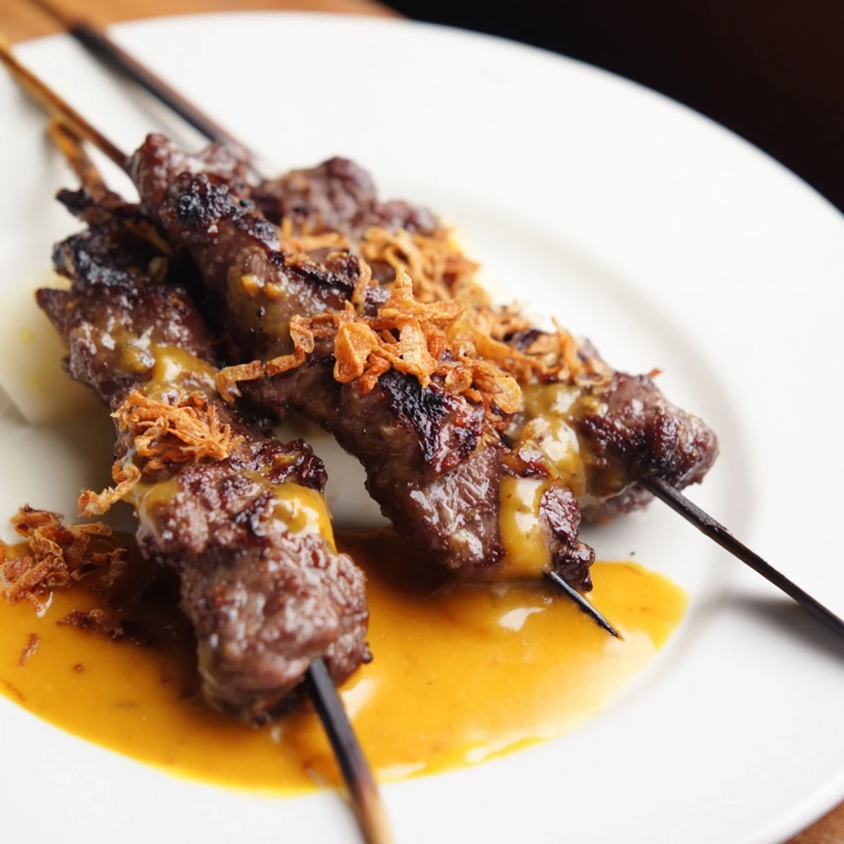Sate Padang beef skewers grilled to charred perfection with thick golden turmeric sauce poured generously over the meat
