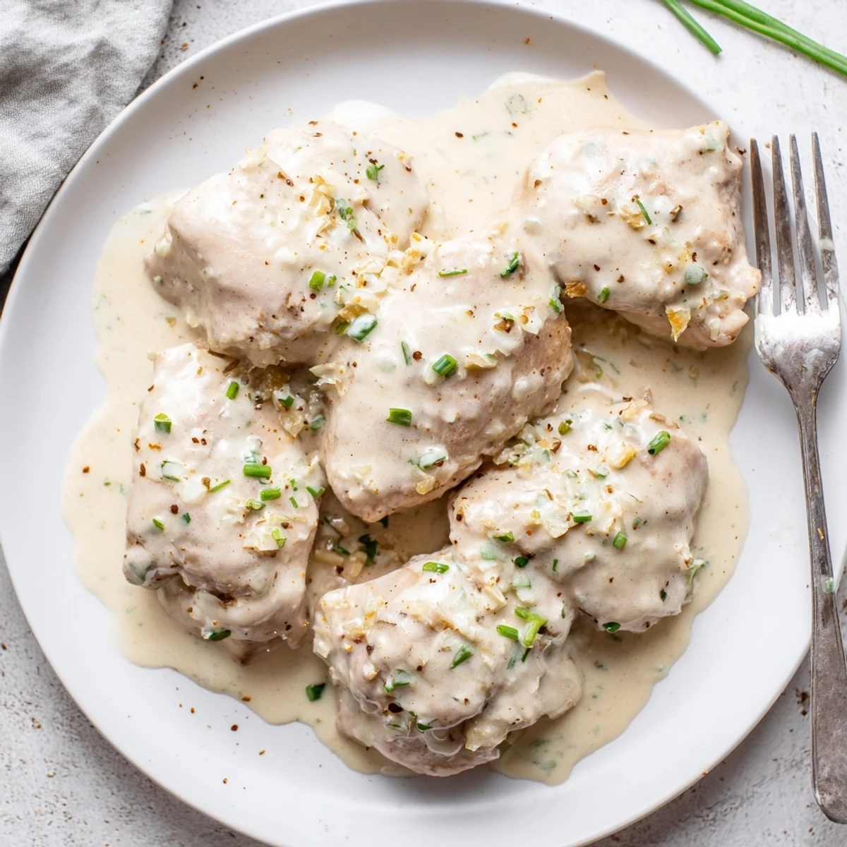 Golden brown chicken thighs swimming in a rich, velvety gravy with herbs and tender onion pieces.
