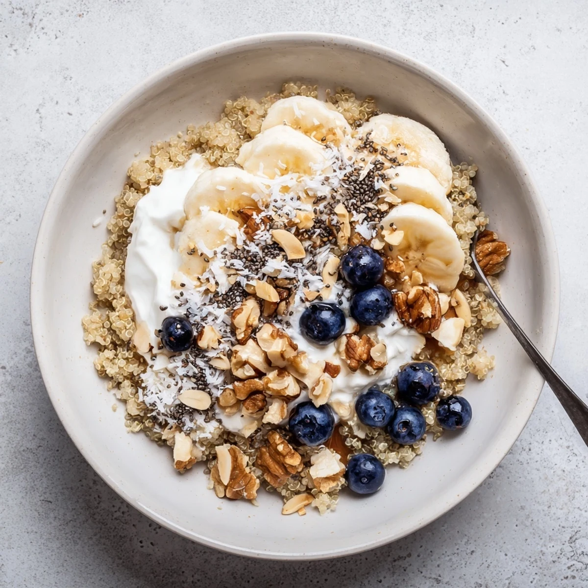 Creamy blueberry quinoa breakfast bowl arranged with Greek yogurt, chia seeds, and shredded coconut garnish on wooden table
