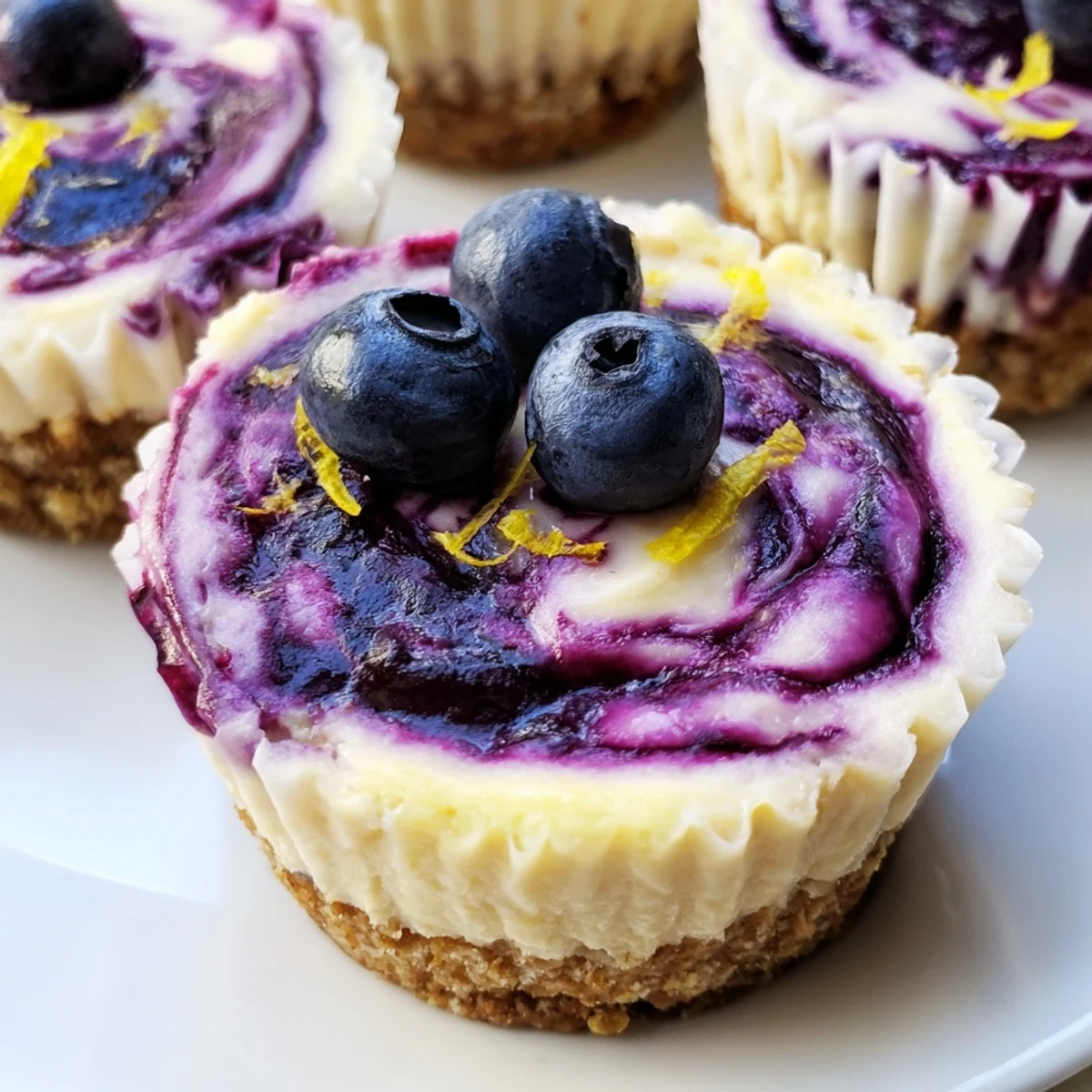 Golden mini lemon blueberry cheesecakes topped with swirled berry compote and fresh zest