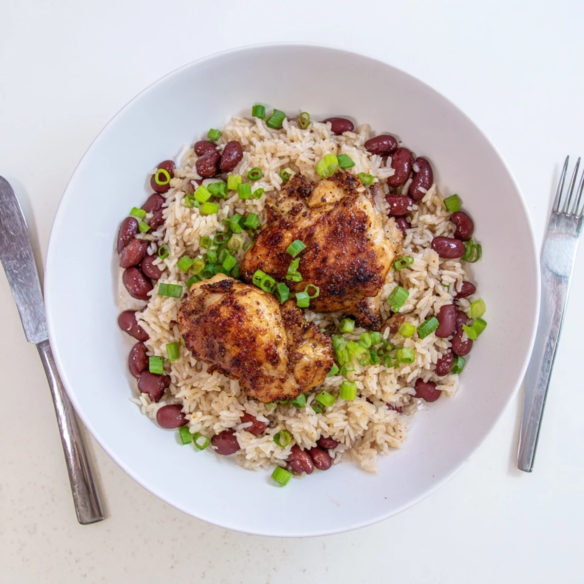 Golden brown jerk chicken thighs with crispy skin resting over fluffy coconut rice speckled with red kidney beans