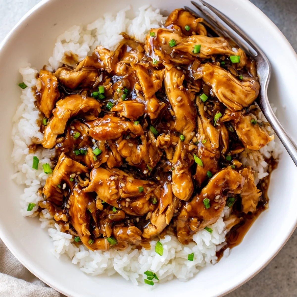 Crockpot Honey Garlic Chicken glistening in sticky sauce, shredded and served over rice