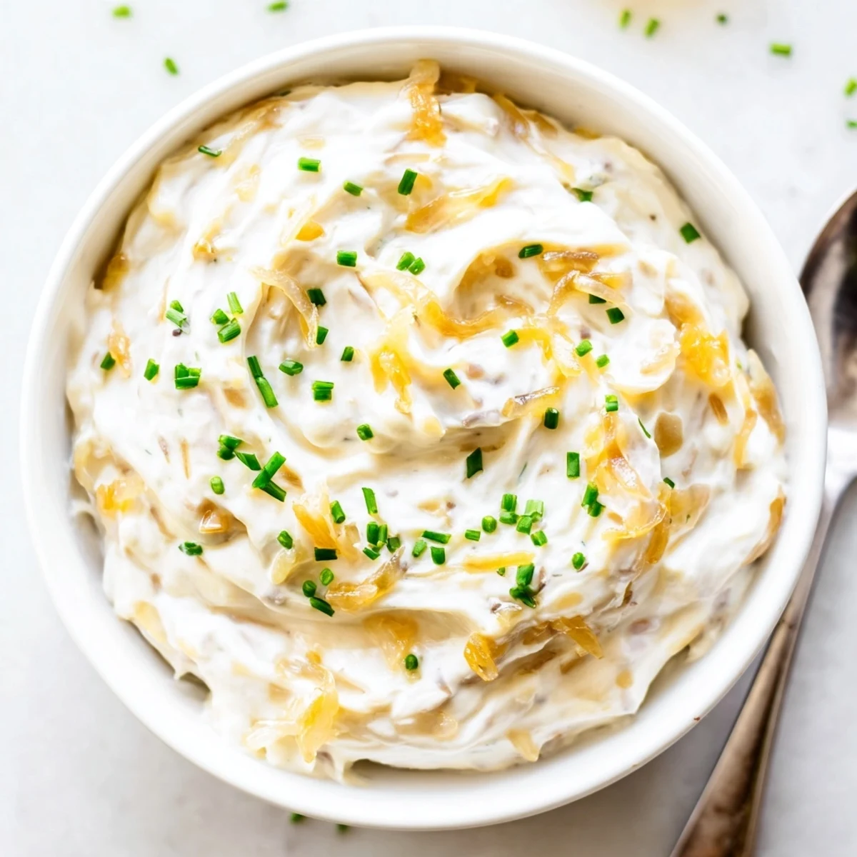 Creamy homemade French onion dip topped with golden caramelized onions and fresh chives in a white serving bowl