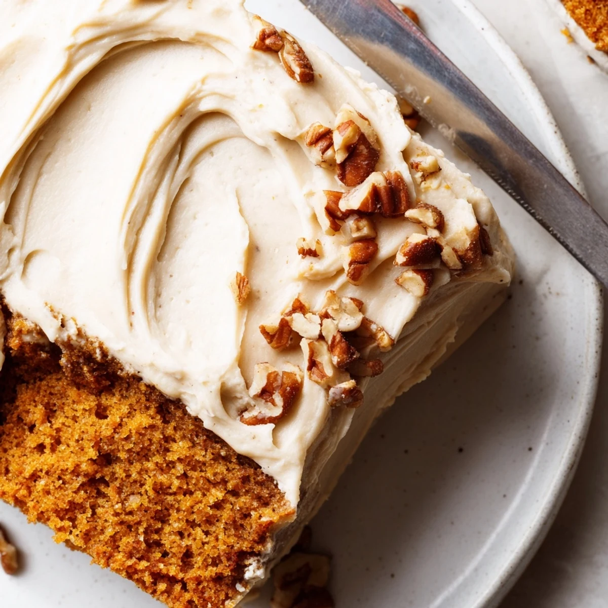 A warm slice of pumpkin pecan cake topped with thick cinnamon cream cheese icing on a rustic plate.