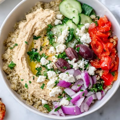 A healthy Mediterranean Quinoa Bowl with Hummus, showing fresh cucumbers, spinach, and a drizzle of lemon dressing.