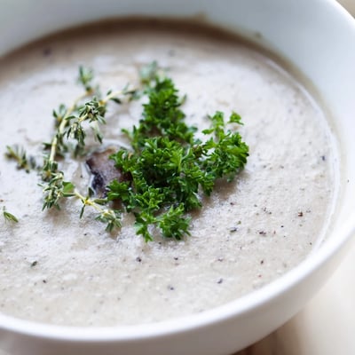 A bowl of creamy mushroom soup with thyme garnished with fresh parsley and crusty bread.