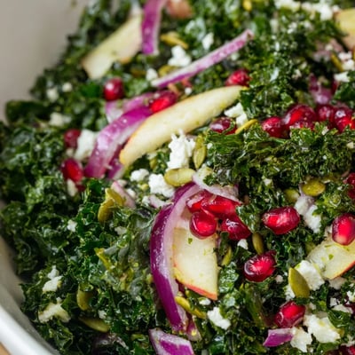 Glistening citrus dressing drizzled over a vibrant Winter Kale Salad with pomegranate seeds and crumbled feta cheese.