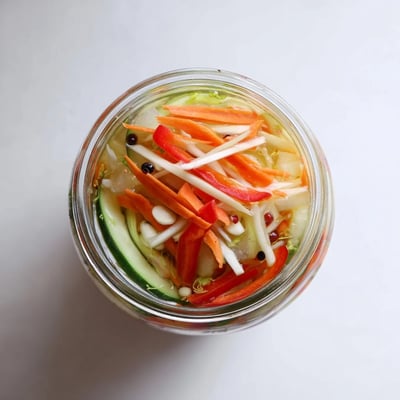 A glass jar displays colorful pickled cucumber and peppers, a crisp Vietnamese Vegetable Pickle Medley side.  