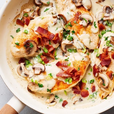A close-up of Mississippi Mud Chicken with bubbly melted cheese, crispy bacon bits, and fresh green onions garnish served over a bed of fluffy white rice.