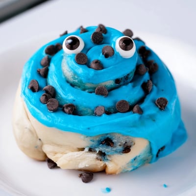 Perfectly risen blue Cookie Monster Cinnamon Rolls are ready to serve, showcasing rich cinnamon filling and chocolate chips inside every soft, warm roll. 