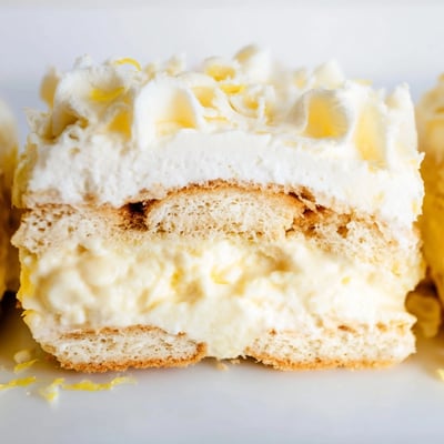No-bake lemon tiramisu garnished with white chocolate curls on a chilled dessert plate