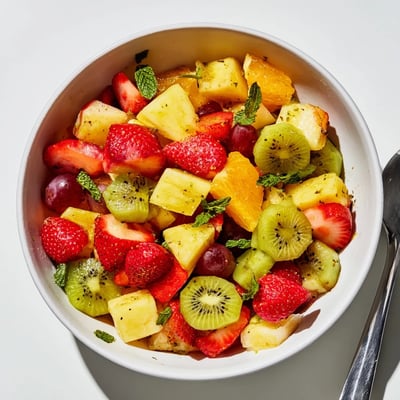 Refreshing fruit bowl drizzled with zesty lime dressing in white serving dish